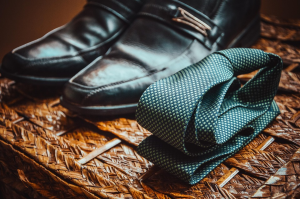 Une paire de chaussures noires cirées et une cravate bleu pétrole roulée