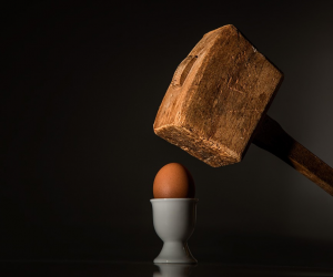 Un gros marteau en bois au-dessus d'un œuf dans un coquetier